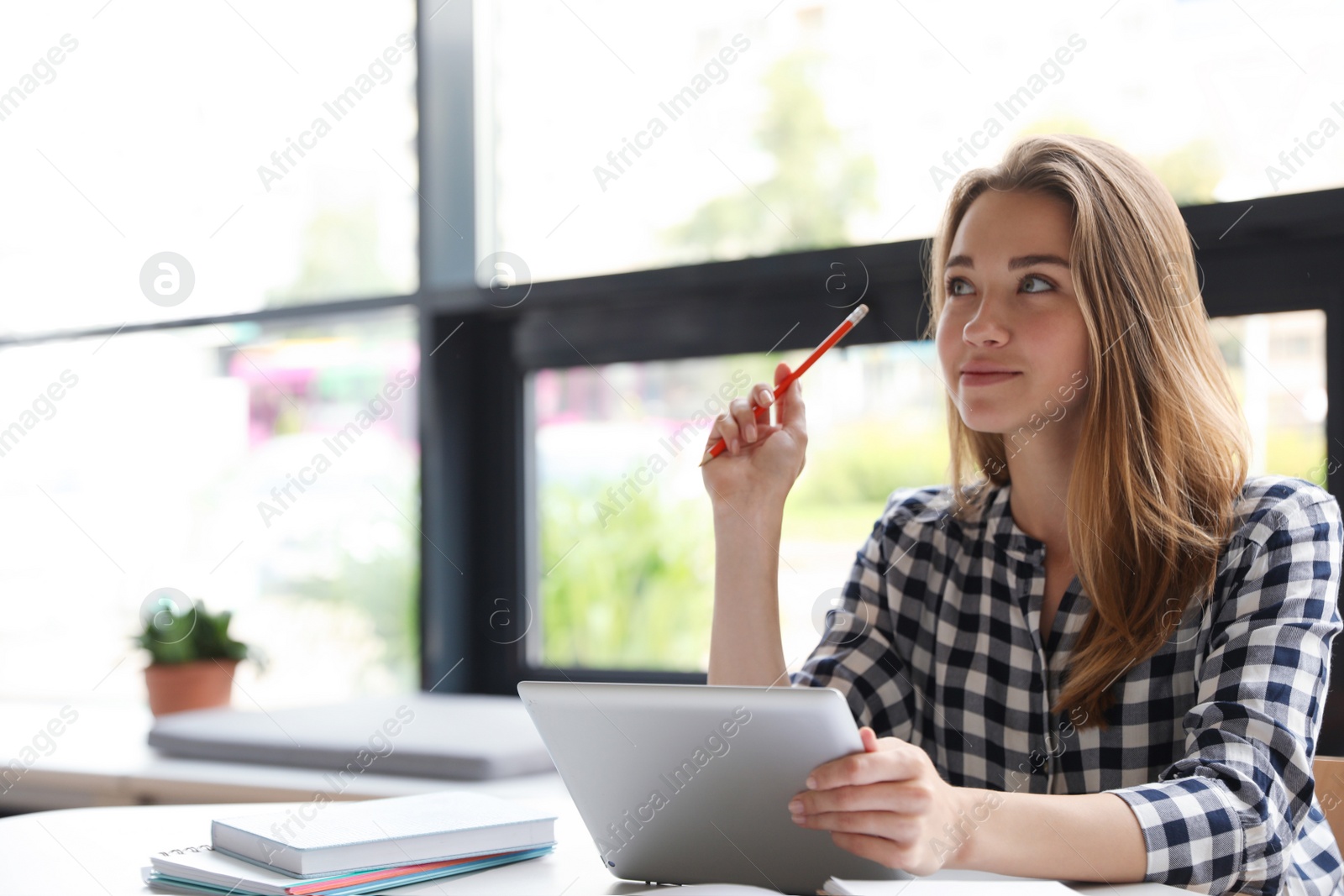 Photo of Pensive young woman studying with tablet at table in library. Space for text