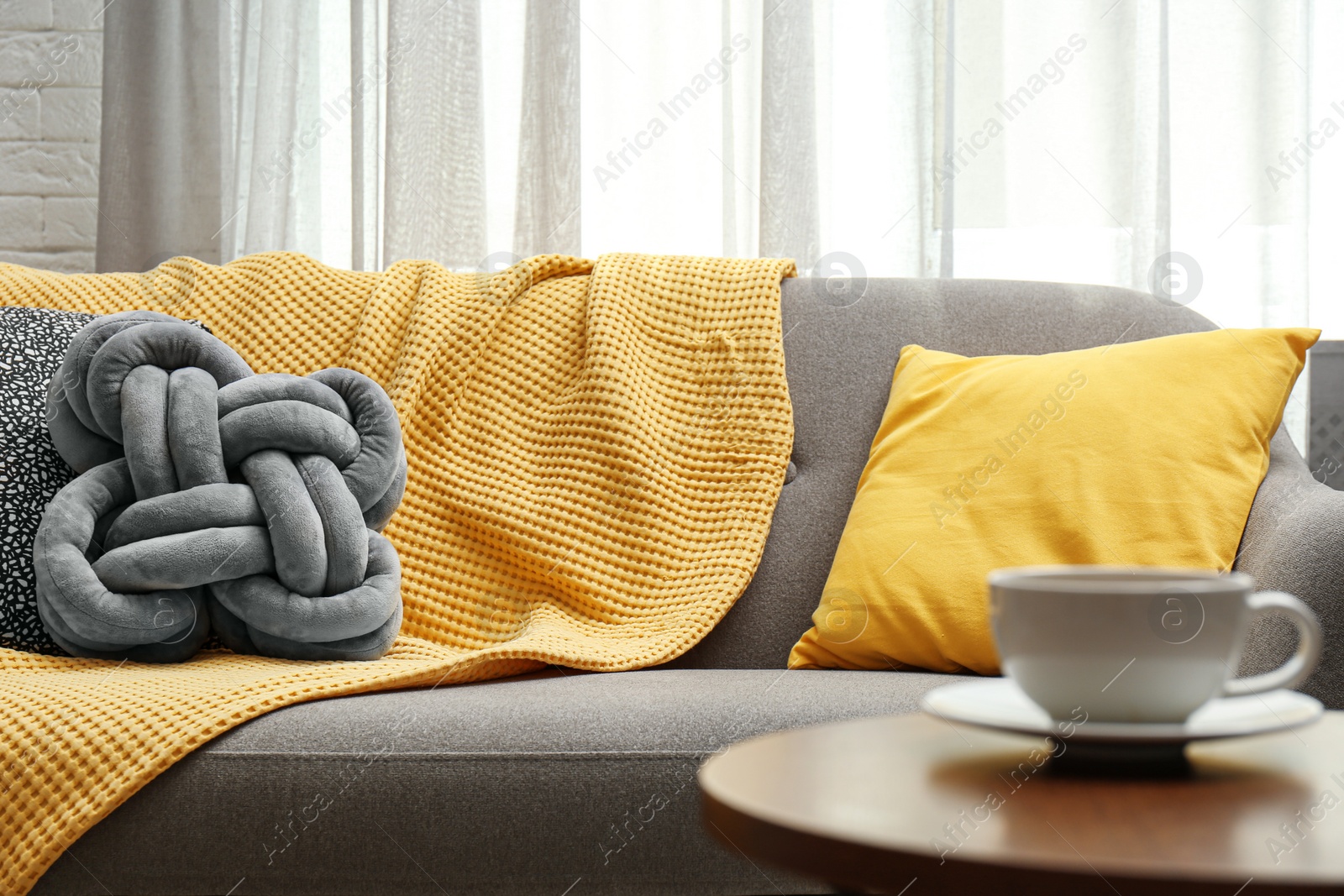 Photo of Soft pillows and yellow plaid on sofa in living room