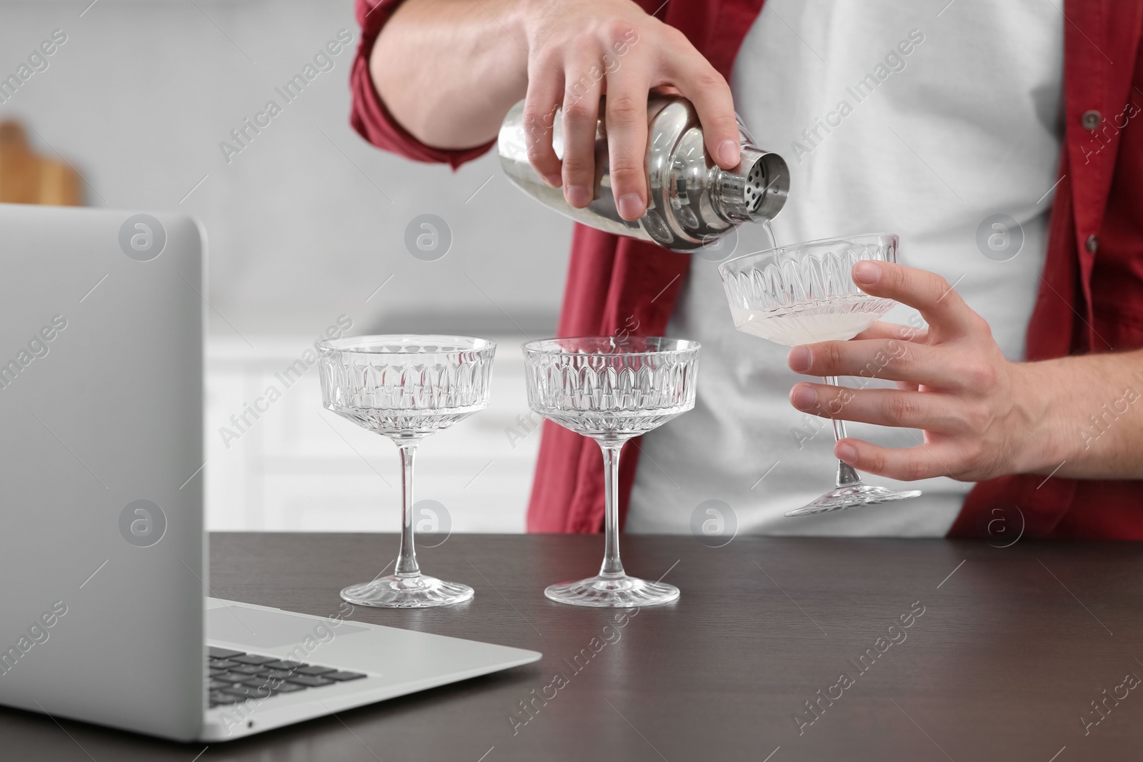 Photo of Man learning to make cocktail with online video on laptop at wooden table in kitchen, closeup. Time for hobby