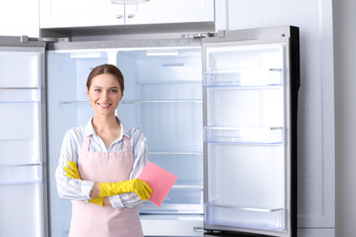 Photo of Woman with rag near clean refrigerator at home