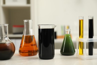 Laboratory glassware with different types of crude oil on light marble table