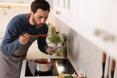 Photo of Man tasting delicious tomato soup in kitchen