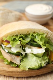 Photo of Delicious pita sandwich with chicken breast and vegetables on wooden table, closeup