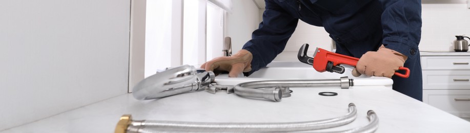 Image of Professional plumber fixing water tap in kitchen, closeup. Banner design