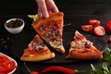 Photo of Woman taking piece of delicious pizza Diablo at black wooden table, closeup