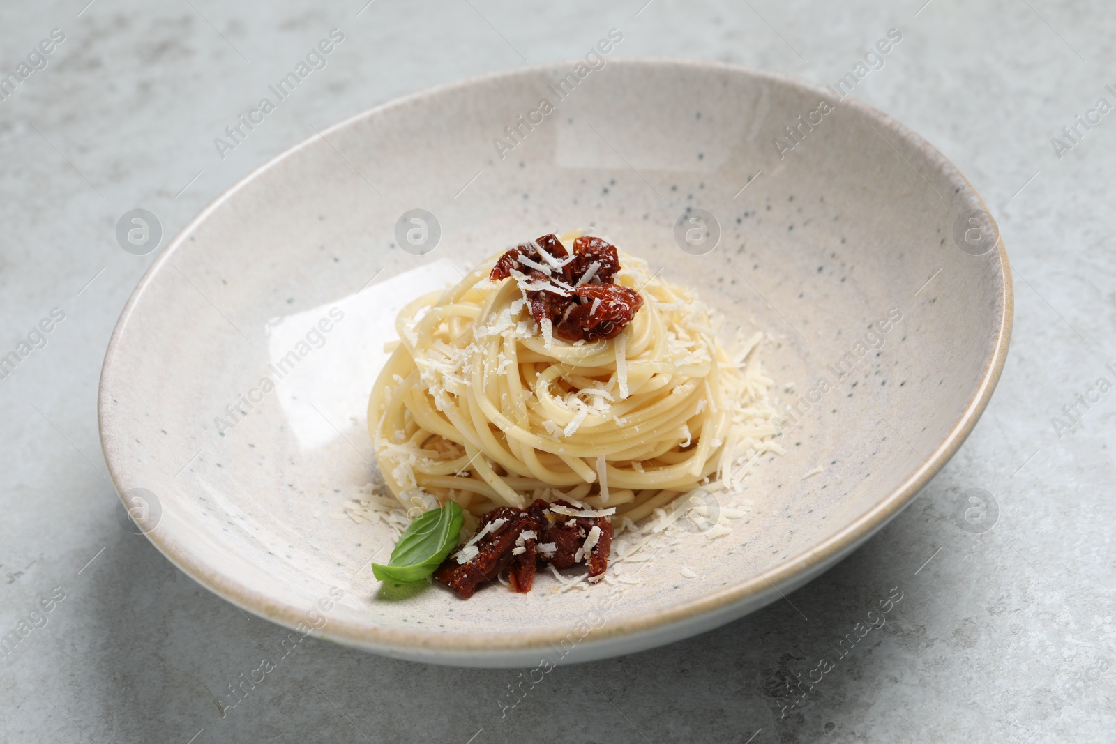 Photo of Tasty spaghetti with sun-dried tomatoes and cheese served on light grey table, closeup. Exquisite presentation of pasta dish