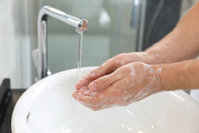 Photo of Man washing hands with soap over sink in bathroom, closeup