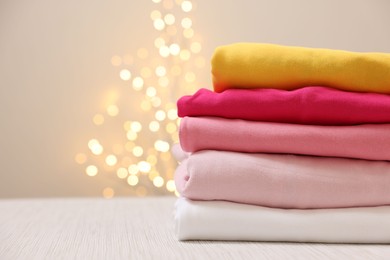 Photo of Stack of folded clothes on wooden table against beige background with blurred lights, space for text