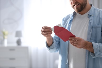 Photo of Man holding envelope with greeting card at home, closeup