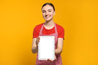 Photo of Beautiful young woman in clean striped apron with tablet on orange background