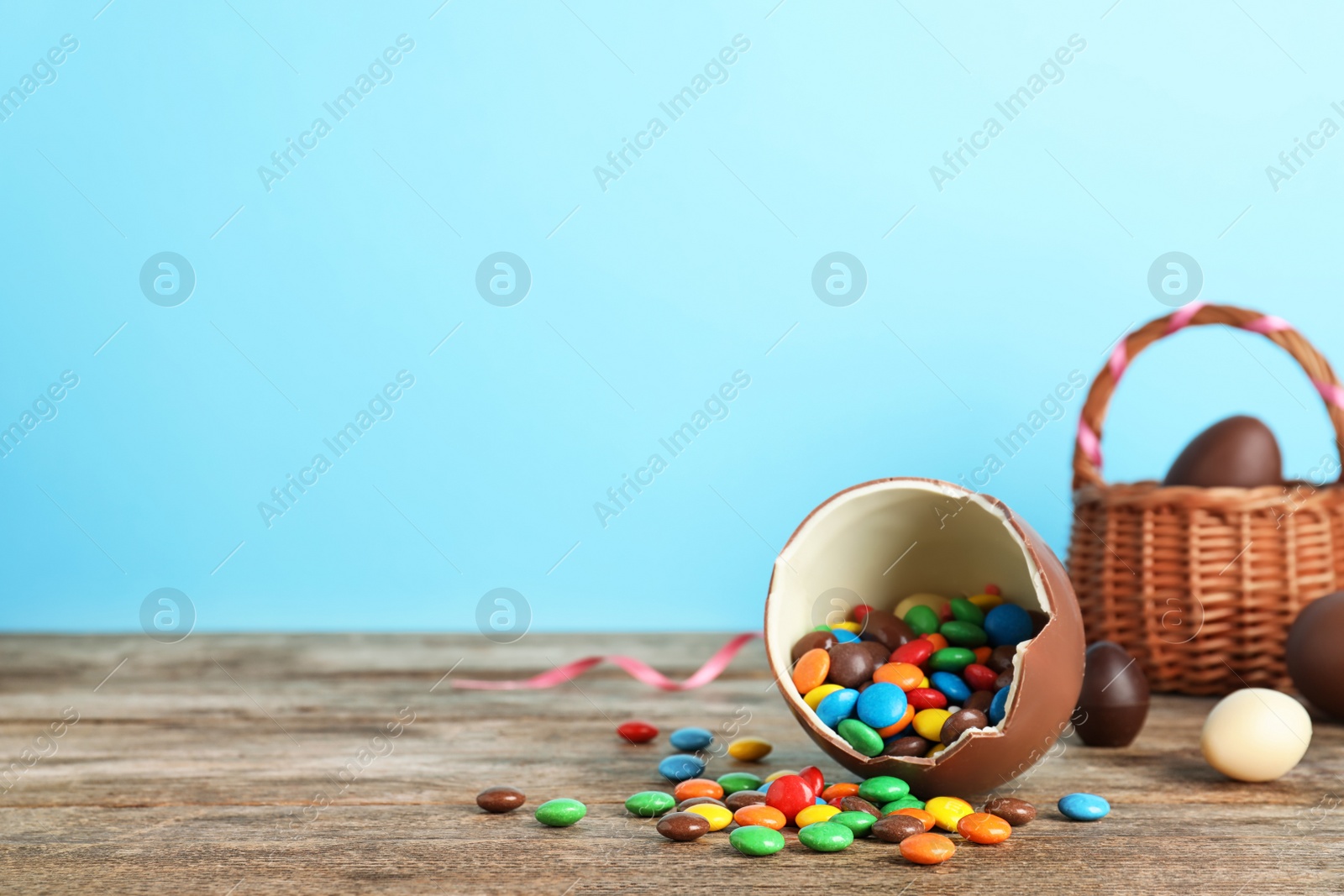 Photo of Broken chocolate Easter egg with candies on wooden table. Space for text