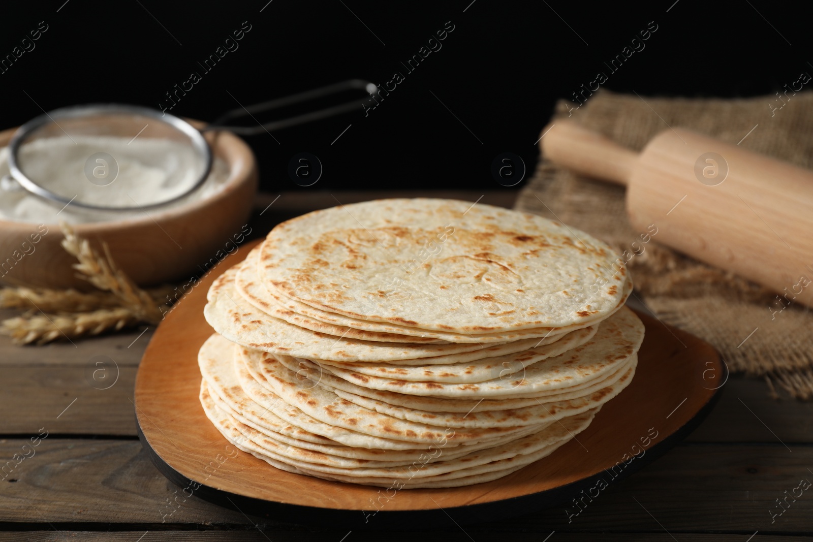 Photo of Many tasty homemade tortillas and rolling pin on wooden table