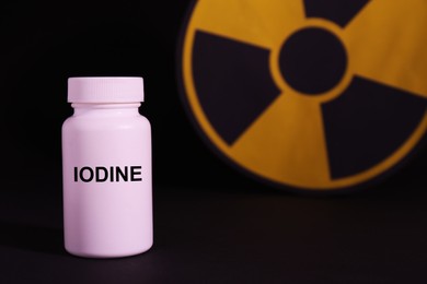 Plastic container of medical iodine and radiation sign on black background, space for text