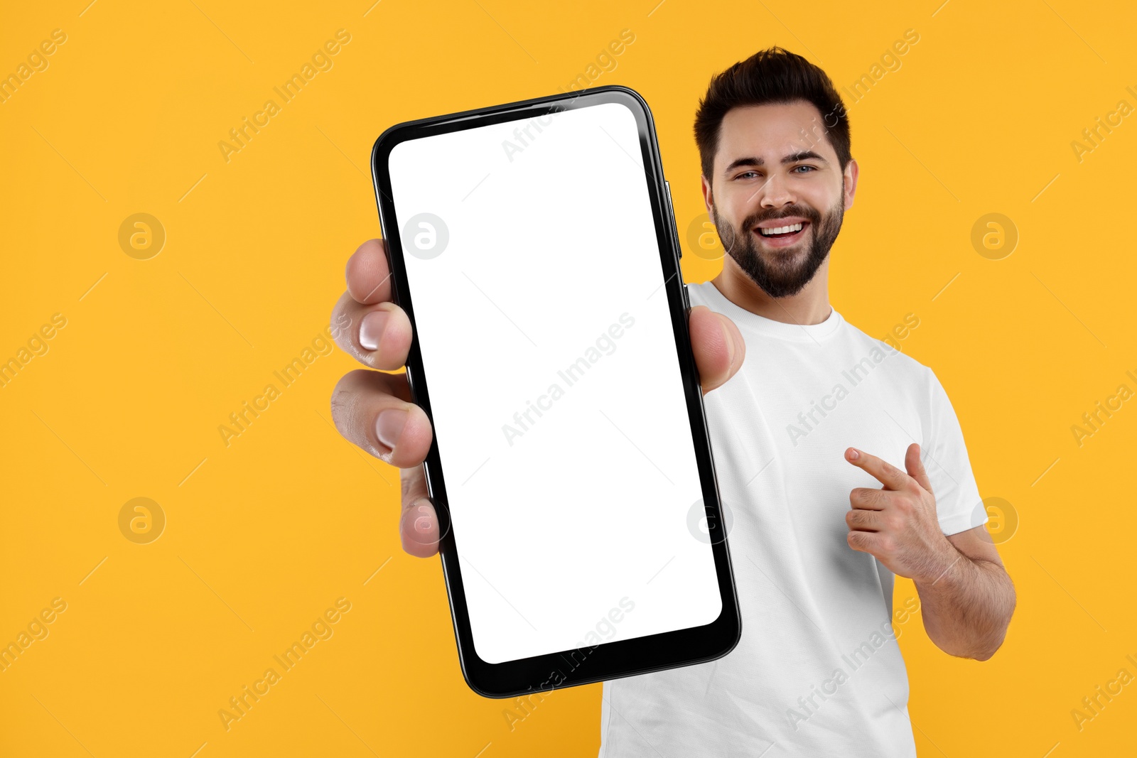 Image of Happy man holding smartphone with empty screen on orange background