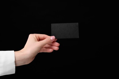 Woman holding blank business card on black background, closeup. Space for text