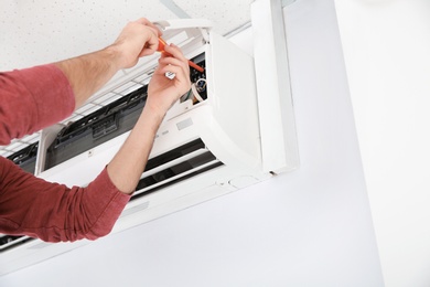 Photo of Electrician with screwdriver repairing air conditioner indoors, closeup. Space for text