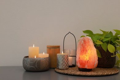 Photo of Himalayan salt lamp, houseplant and candles on grey table near light wall, space for text