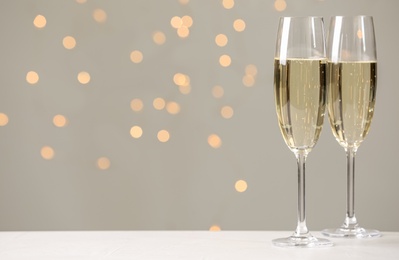 Photo of Glasses of champagne on grey table against blurred lights. Space for text