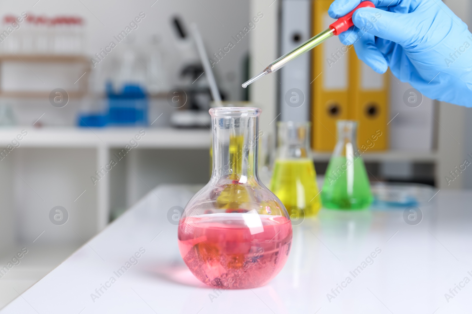 Photo of Laboratory analysis. Woman dripping liquid into flask at white table, closeup