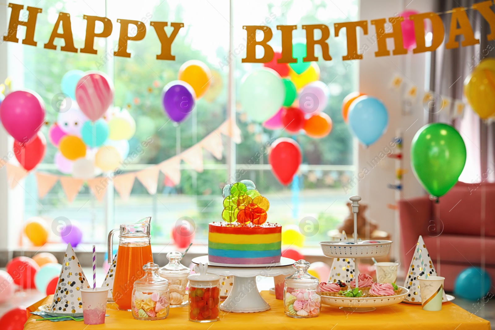 Photo of Bright birthday cake and other treats on table in decorated room