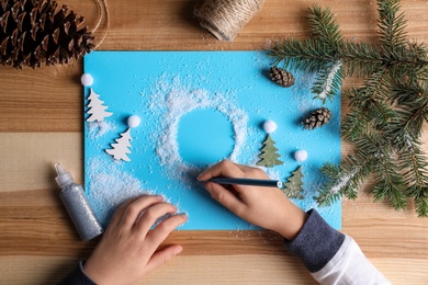 Photo of Little child making Christmas card at wooden table, top view