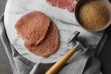 Photo of Cooking schnitzel. Raw pork chops in bread crumbs and meat mallet on grey table, top view