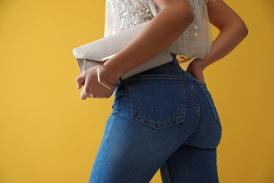 Photo of Woman in jeans with clutch purse on yellow background, closeup