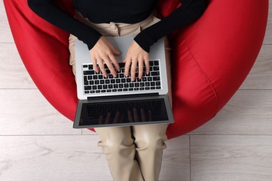 Photo of Woman working with laptop in beanbag chair, top view