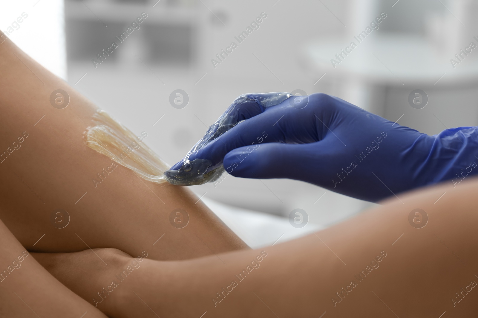 Photo of Woman getting wax epilation of legs in salon, closeup