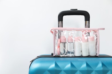 Photo of Cosmetic travel kit in plastic bag on suitcase against light background, space for text