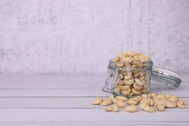 Photo of Glass jar with tasty cashew nuts on white wooden table. space for text