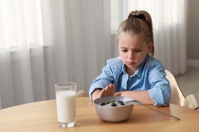 Photo of Cute little girl refusing to eat her breakfast at home, space for text