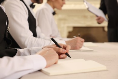 People writing notes in notebooks at table during lecture, closeup. Professional butler courses