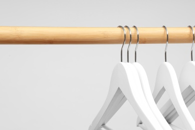 Photo of Empty clothes hangers on wooden rail against light background, closeup. Space for text