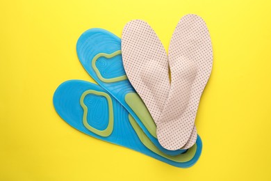 Photo of LIght blue and beige orthopedic insoles on yellow background, flat lay