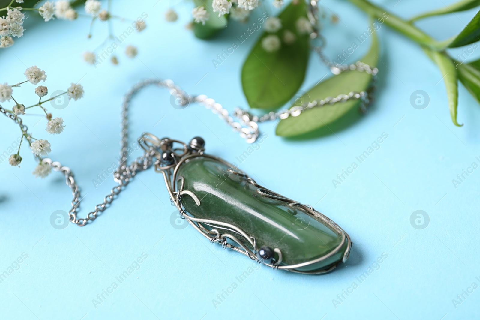 Photo of Beautiful silver necklace with nephrite gemstone and flowers on light blue background