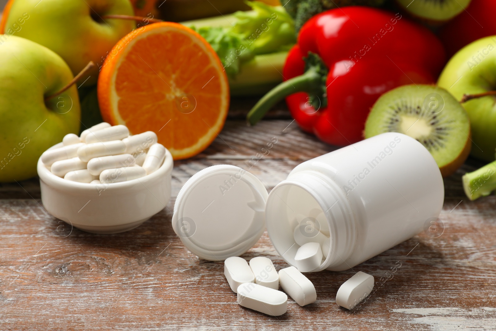 Photo of Dietary supplements. Overturned bottle, pills and food products on wooden table, closeup