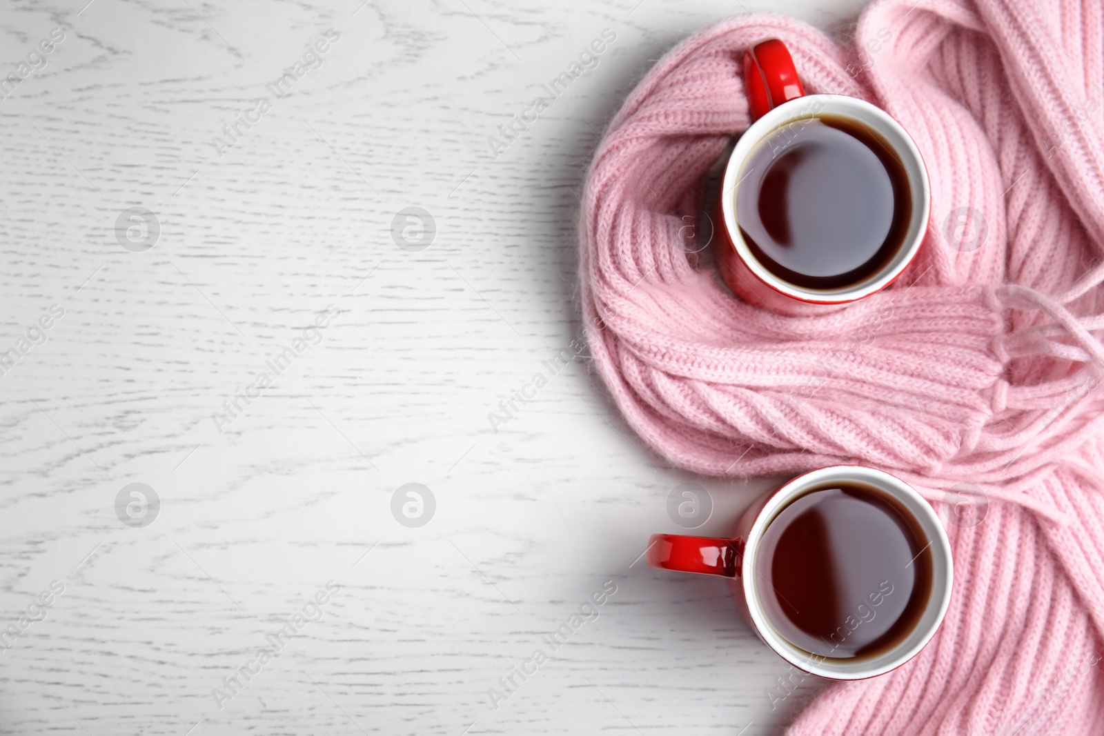 Photo of Flat lay composition cups of hot tea and knitted scarf on white wooden background, space for text. Winter drink