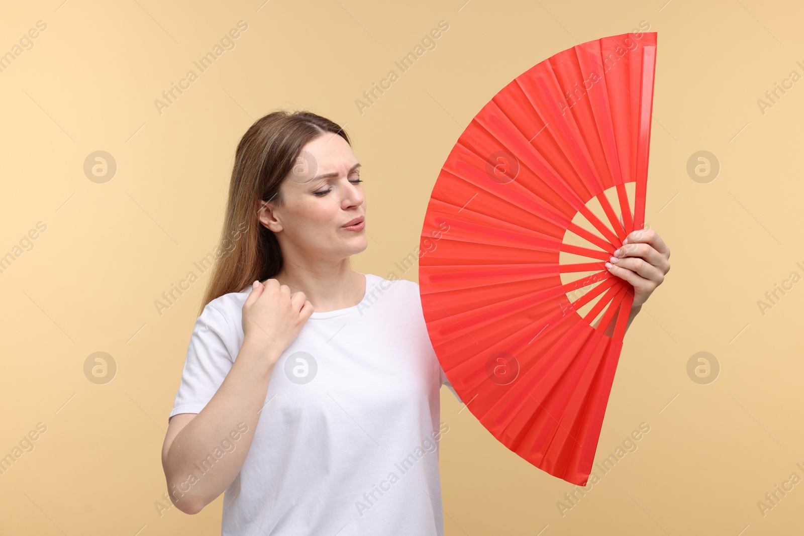 Photo of Beautiful woman waving red hand fan to cool herself on beige background