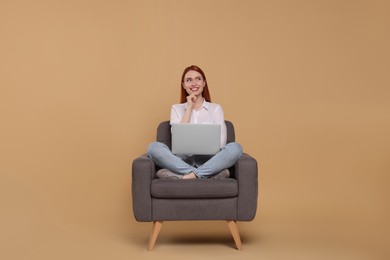 Photo of Smiling young woman with laptop sitting in armchair on beige background