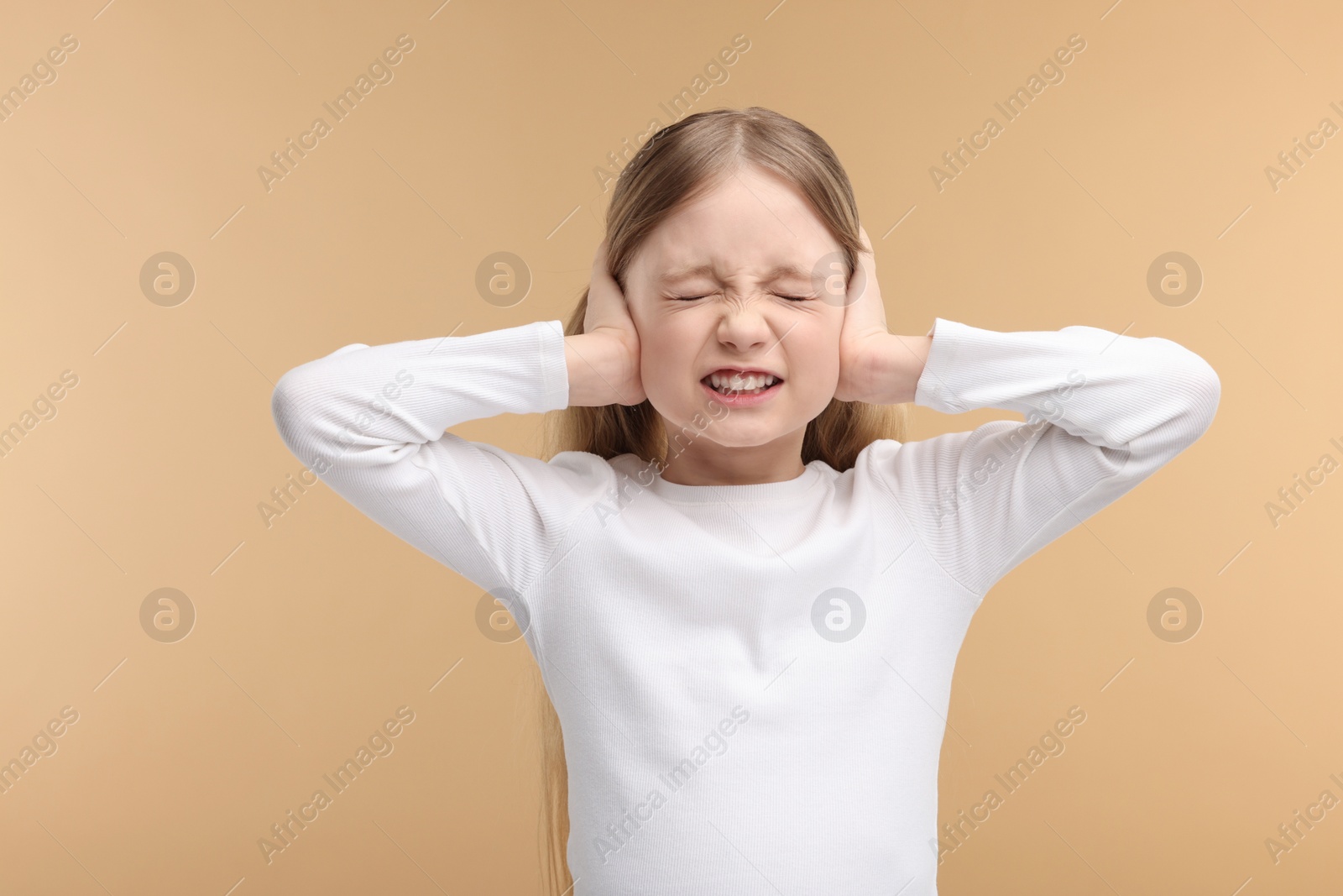 Photo of Hearing problem. Little girl suffering from ear pain on pale brown background