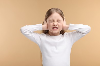 Hearing problem. Little girl suffering from ear pain on pale brown background