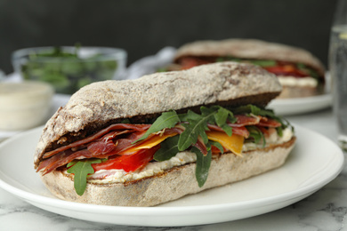 Photo of Delicious sandwich with fresh vegetables and prosciutto on white marble table