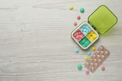Photo of Plastic box and different pills on wooden table, flat lay. Space for text