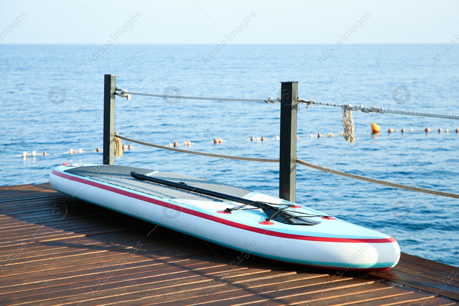 Photo of SUP board with paddle on wooden pier near sea