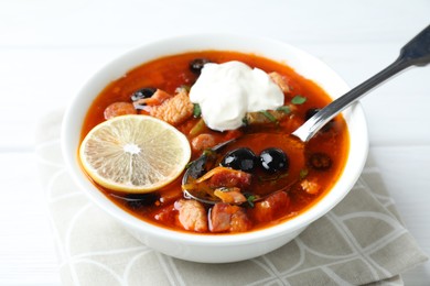 Meat solyanka soup with sausages, olives, vegetables and spoon on white table, closeup