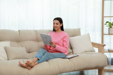 Photo of Young woman coloring antistress page on sofa in living room