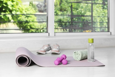 Photo of Exercise mat, dumbbells, towel, bottle of water and shoes on floor indoors