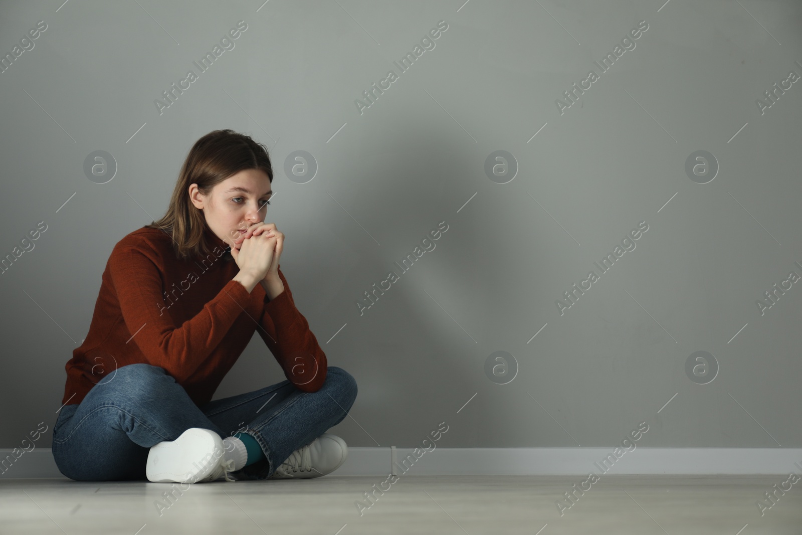 Photo of Sad young woman sitting on floor near grey wall indoors, space for text