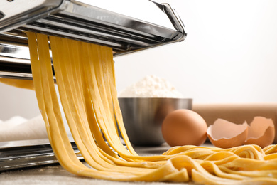 Photo of Pasta maker machine with dough on grey table, closeup